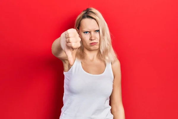 カジュアルな白いTシャツを着た美しい白人ブロンドの女性は 親指を下にジェスチャーで拒絶と否定を示す不満と怒りを見ています 悪い表現 — ストック写真