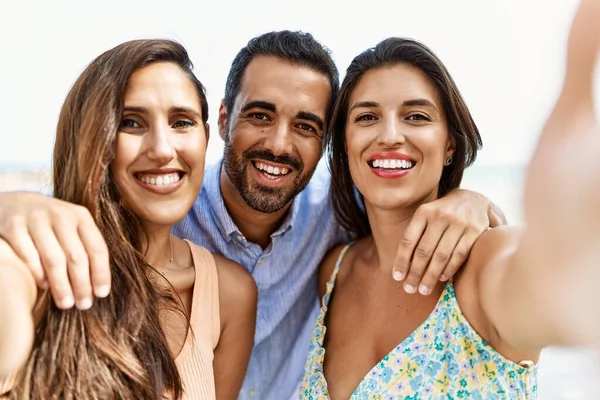 stock image Three young hispanic friends smiling happy and hugging make selfie by the camera at the beach.