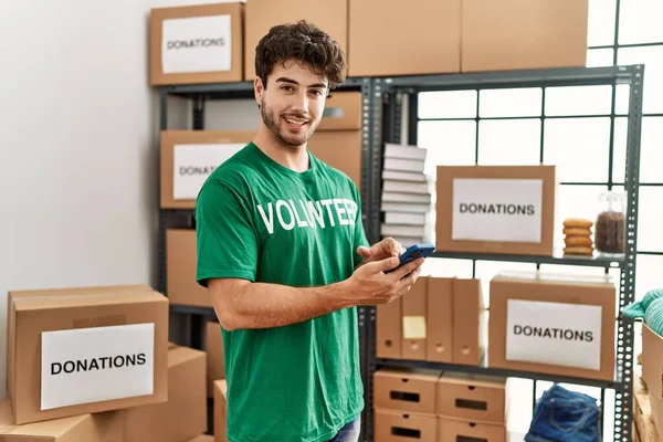 Jonge Spaanse Man Vrijwilligersuniform Met Smartphone Een Liefdadigheidscentrum — Stockfoto