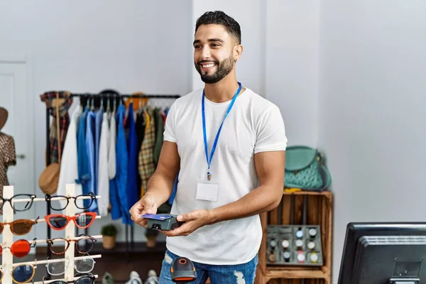 衣料品店でクレジットカードやデータ電話で支払う若いアラブ人の男店主 — ストック写真