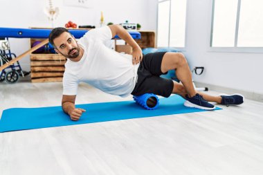 Genç İspanyol hasta klinikte köpük silindir kullanarak bacak rehabilitasyonu seansı yapıyor.