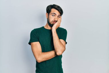 Günlük beyaz tişört giyen genç İspanyol adam çapraz kollu depresyondan sıkılmış ve yorgun görünüyor.. 