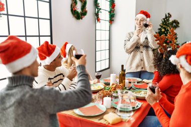Mutlu bir şekilde gülümseyen bir grup genç Noel yemeği yiyor ve evde kadeh kaldırıyor..