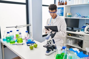 Laboratuvarda panoya yazı yazan, bilim adamı üniforması giyen İspanyol bir genç.