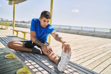 Genç İspanyol adam dışarıda bacak kaslarını esnetiyor.