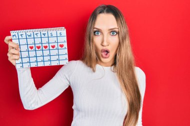 Kalp takvimi tutan genç sarışın kız. Korkmuş ve ağzı açık kalmış, şaşırmış ve şaşırmış. Şaşırmış. 