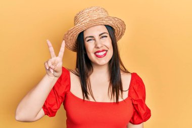 Genç İspanyol kadın yaz şapkası takıyor ve iki numarayı gösterip işaret ederken kendinden emin ve mutlu gülümsüyor.. 