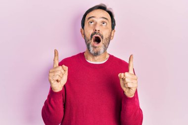 Orta yaşlı, sıradan kıyafetler giyen, şaşkın şaşkın bakan, parmaklarıyla işaret eden ve kollarını kaldıran bir İspanyol.. 