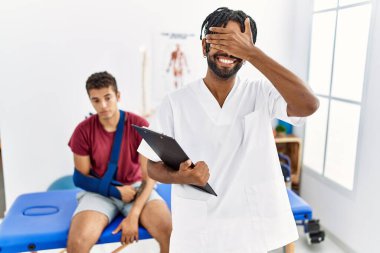 Kırık kollu bir adamla birlikte acı giderme kliniğinde çalışan genç bir İspanyol. Gülümseyen ve gülen bir adam. kör kavram. 
