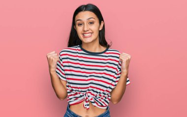 Gündelik giysiler giyen genç İspanyol kız kollarını kaldırıp, gözleri açık bir şekilde başarıyı kutluyor ve şaşırıyor. Kazanan konsept. 