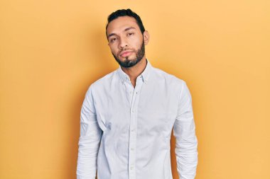 Sakallı, iş gömleği giyen İspanyol bir adam. Yüzünde ciddi bir ifadeyle rahatlamış. Basit ve doğal bir şekilde kameraya bakıyorsun.. 