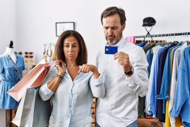 İspanyol orta yaşlı çift ellerinde alışveriş torbaları ve kredi kartı var üzgün ve üzgün görünüyorlar, parmaklarıyla yön gösteriyorlar, mutsuz ve depresif.. 