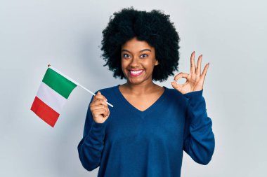 Genç Afro-Amerikan kadını elinde İtalya bayrağı tutarken parmaklarıyla işaret veriyor, gülümseyerek mükemmel bir sembol oluşturuyor. 