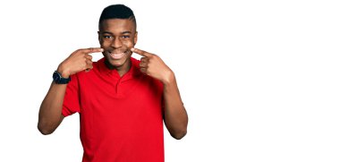 Gündelik kırmızı tişört giyen, gülümseyen, parmaklarıyla ve ağzıyla işaret eden Afro-Amerikan genç adam. diş sağlığı kavramı. 