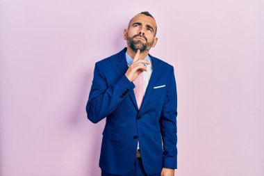 Genç İspanyol bir adam iş elbisesi ve kravat takıyor. Düşüncelerini şüpheye odaklıyor. Parmakları çenesinde ve yukarı bakıyor. 