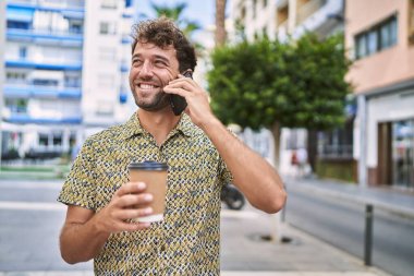 Genç İspanyol adam akıllı telefonda konuşuyor. Sokakta kahve içiyor.