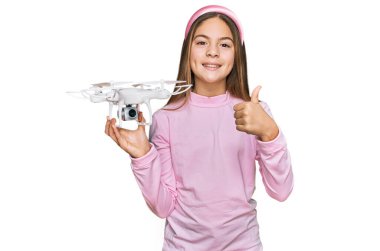 Güzel esmer küçük kız mutlu ve pozitif gülümseyen drone kullanıyor, başparmağı mükemmel ve onay işareti yapıyor. 