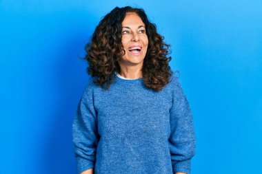 Orta yaşlı İspanyol kadın gündelik kıyafetler giyip yüzünde gülümsemeyle yan yana bakıyor, doğal bir ifade. Kendinden emin gülen. 