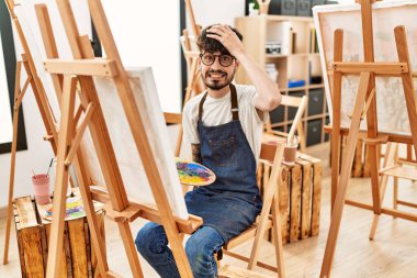 Resim stüdyosundaki sakallı İspanyol adam elleri kafasında, şaşırmış ve sinirli yüzüyle stresli ve hayal kırıklığına uğramış. 