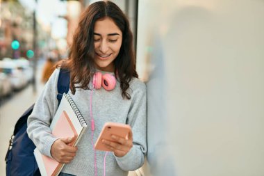 Genç ortadoğulu kız şehirde akıllı telefon kullanarak mutlu bir şekilde gülümsüyor..