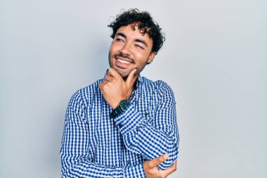 Elleri çenesinde gündelik giysiler içinde soru soran genç İspanyol bir adam, düşünceli bir ifade. Düşünceli bir yüzle gülümsüyor. şüphe kavramı. 