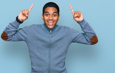 Genç, yakışıklı, sıradan bir eşofman üstü giyen, şaşkın, şaşkın, parmaklarıyla işaret eden ve kollarını kaldıran bir adam.. 