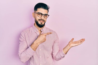 Sakallı, sıradan gömlekli ve gözlüklü yakışıklı adam kameraya hayret ediyor ve gülümsüyor.. 