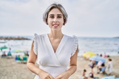 Kumsalda mutlu mutlu gülümseyen beyaz bir kız..
