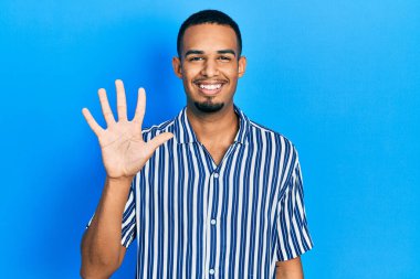 Genç Afro-Amerikalı günlük kıyafetler giymiş beş numarayı gösterip işaret ederken kendinden emin ve mutlu bir şekilde gülümsüyor.. 