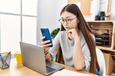 Genç Asyalı kadın ofiste akıllı telefon kullanıyor.