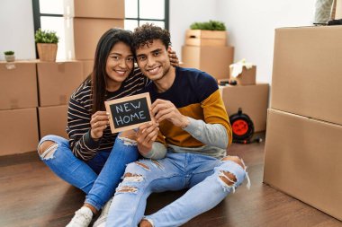 Genç Latin çift yeni ev tahtasıyla yerde oturuyorlar..