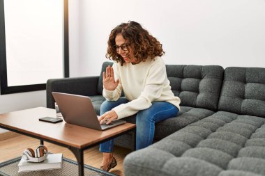 Orta yaşlı İspanyol bir kadın evde video araması yaptığından emin bir şekilde gülümsüyor.