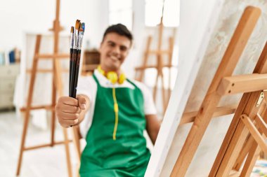 Resim stüdyosunda kendine güvenen, gülümseyen İspanyol genç bir adam.