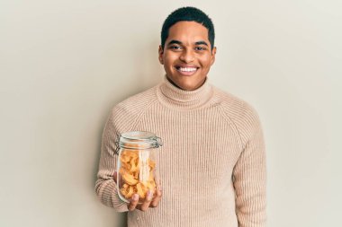 Genç, yakışıklı İspanyol adam elinde makarna kavanozuyla pozitif ve mutlu görünüyor. Kendine güvenen bir gülümsemeyle dişlerini gösteriyor. 