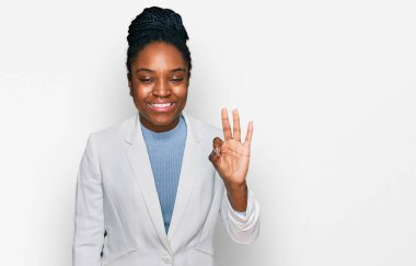 Genç afro-amerikan kadın iş kıyafetleri giyip üç numaralı parmaklarıyla işaret ederken kendinden emin ve mutlu bir şekilde gülümsüyor.. 