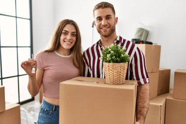 Genç beyaz çift mutlu bir şekilde gülümsüyor. Karton kutu ve yeni evin anahtarını tutuyorlar..