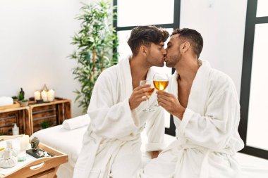 İki İspanyol erkeği, güzellik merkezindeki masaj masasında şampanyayla öpüşüp kadeh kaldırıyor.