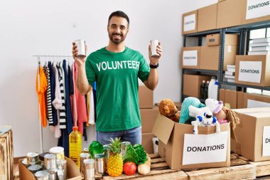 Gönüllü üniformalı genç İspanyol bir adam yardım merkezinde konserve yiyecek tutuyor.