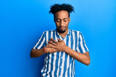 Sakallı, sıradan çizgili tişörtlü, göğsünde elleri kapalı, yüzünde minnet dolu bir jest olan Afrikalı genç bir Amerikalı. sağlık kavramı. 
