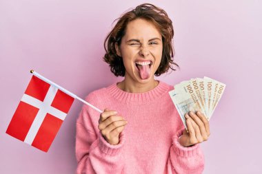 Genç esmer kadın Norveç bayrağı ve krone banknotları taşıyor. Komik bir ifadeyle dillerini dışarı çıkarıyorlar.. 