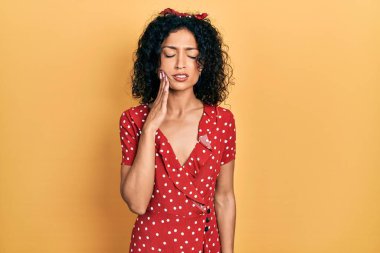 Yazlık elbise giyen genç Latin kız diş ağrısı ya da diş hastalığından dolayı acı dolu bir ifadeyle dudaklarına dokunuyor. dişçi 