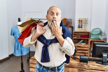 Dükkanda elinde alışveriş poşetleri tutan yakışıklı bir adam ağzı elle kapatıyor, şaşırmış ve hata yapmaktan korkuyor. şaşırmış ifade 