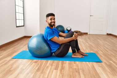 Yakışıklı İspanyol adam egzersiz yapıyor ve yoga minderinde geriniyor, spor salonunda pilates topuyla esneklik gösteriyor.