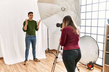 Young man at photography studio celebrating victory with happy smile and winner expression with raised hands 