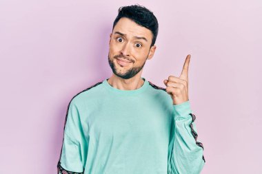 Gündelik kıyafetler giyen genç İspanyol adam başarılı bir fikirle işaret ediyor. Heyecanlı ve mutlu. Bir numara.. 