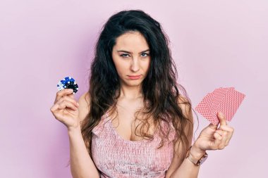 Elinde kumarhane fişleriyle poker oynayan genç İspanyol kadın şüpheci ve gergin, sorun yüzünden surat asıyor. negatif kişi. 