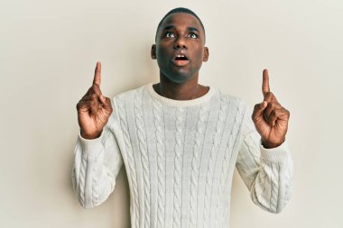 Gündelik giysiler giyen genç Afro-Amerikan adam şaşkın ve şaşırmış bir şekilde yukarı baktı ve parmaklarıyla işaret etti ve kollarını kaldırdı.. 