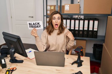 Young beautiful woman holding black friday banner small commerce scared and amazed with open mouth for surprise, disbelief face 
