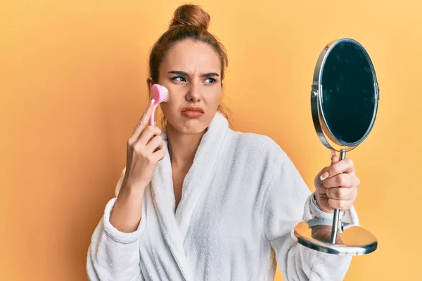 Mujer Rubia Joven Con Bata Sosteniendo Cepillo Removedor Maquillaje Escéptico — Foto de Stock