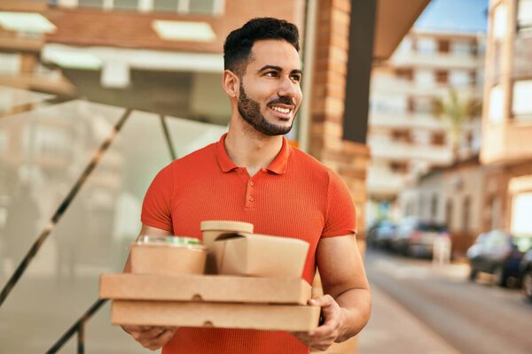 Молодой латиноамериканец улыбается счастливо держа еду в городе.